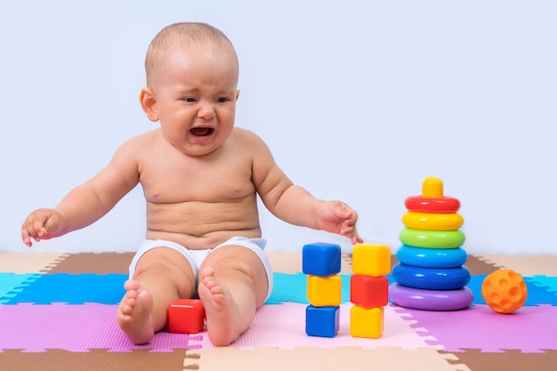 A toddler cries while sitting on the floor in the playroom among toys.