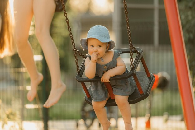 Toddler in a dress is sucking her thumb on a swing on the warm summer evening