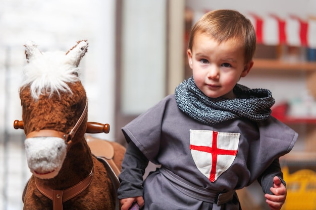 Photo toddler dressed as a knight next to his rocking horse