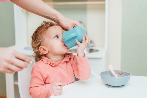 家庭でプラスチック製のコップから水を飲む幼児