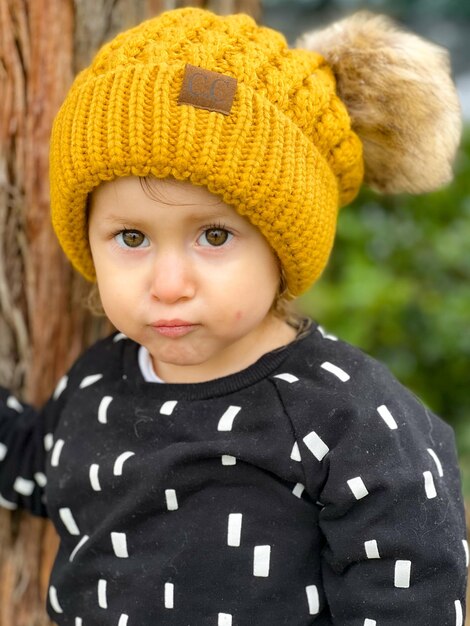 Photo toddler fiercely looking at camera with a beautiful yellow beanie with puffy ears