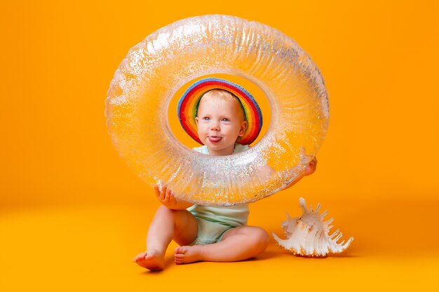 Toddler girl in blue bodysuit and swimming circle sits on a yellow wall