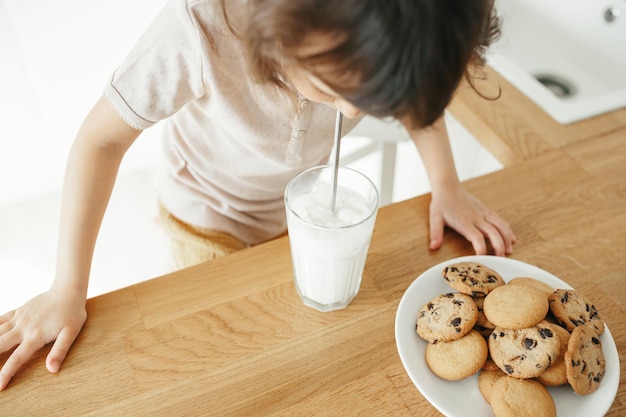 ガラスのストローでミルクを飲む幼児の女の子 子供たちとの持続可能な生活