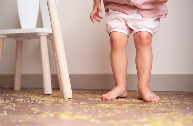 Photo toddler girl legs standing on messy floor after playing with grain nuts pasta and ricesensorial early development education for baby childkids dirty room concept