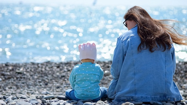 조약돌 해변에 함께 앉아 유아 소녀와 어머니