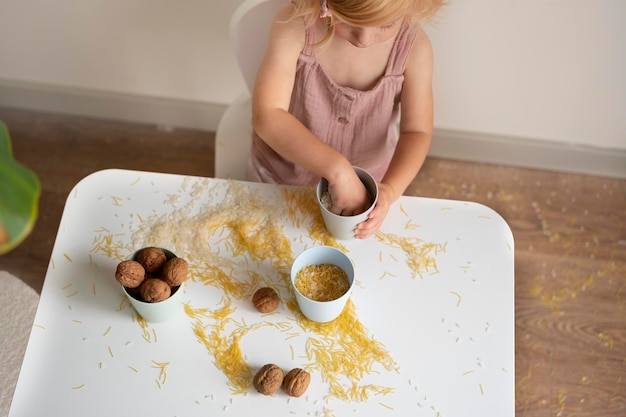 テーブルに座って穀物ナッツパスタとライスで遊ぶ幼児の女の子赤ちゃんの子供のための感覚早期発達教育子供の役に立つゲームトップビュー