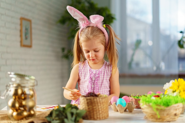 Ragazza del bambino con le orecchie del coniglietto che colora le uova per pasqua