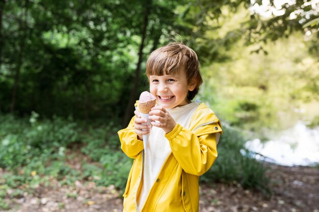 Photo toddler happy boy eating ice cream in a waffle cone outside child wearing yellow light jacket snacking in the park in summer tasty sweet food