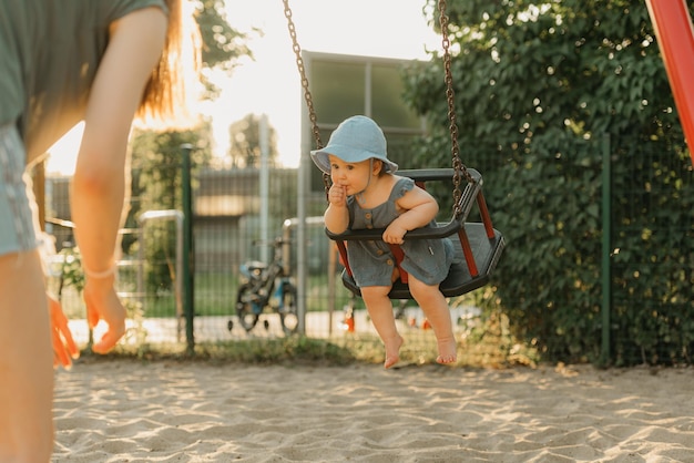 写真 暖かい夏の夜、ドレスを着た幼児がブランコに乗って親指をしゃぶっている