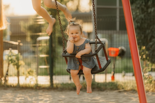 写真 暖かい夏の夜、ドレスを着た幼児がブランコに乗って親指をしゃぶっている