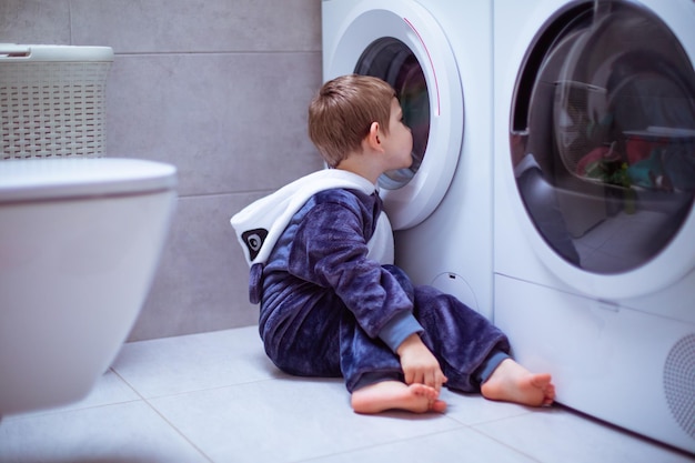 The toddler is looking into the washing machine while wash