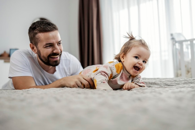 Toddler is playing with her father in a bedroom She is crawling on a bed