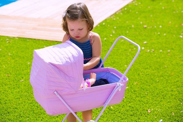 Toddler kid girl playing with baby cart in green turf