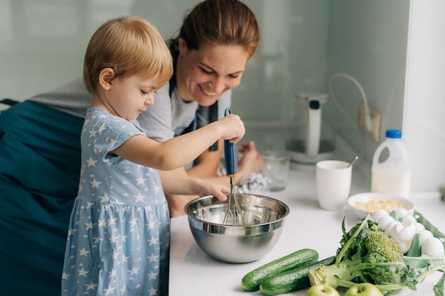 Toddler little daughter helps her mother cook an omelet