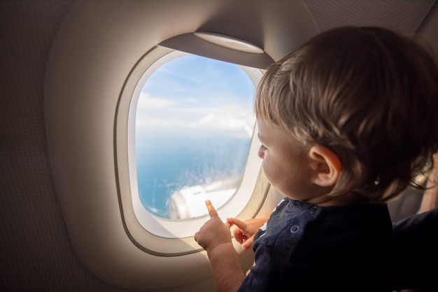 幼児は飛行機の舷窓を通して地面を見ます