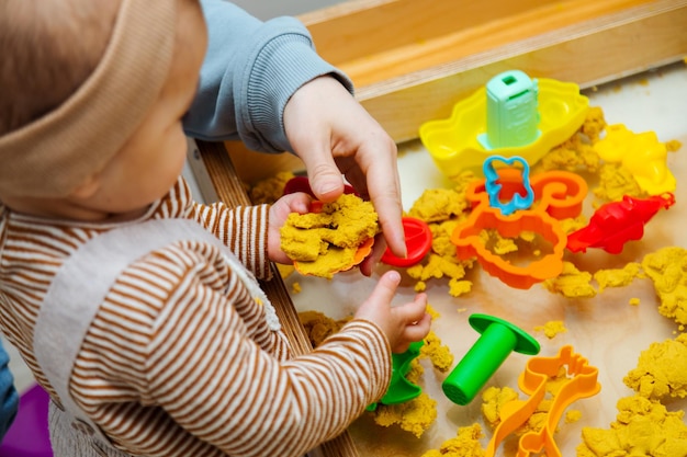 プラスチックの形をしたキネティックサンドで遊ぶ幼児