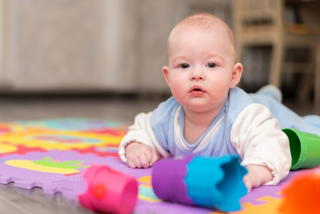 A toddler plays on the floor. The infant is lying on his abdomen on carpet with a pyramid.