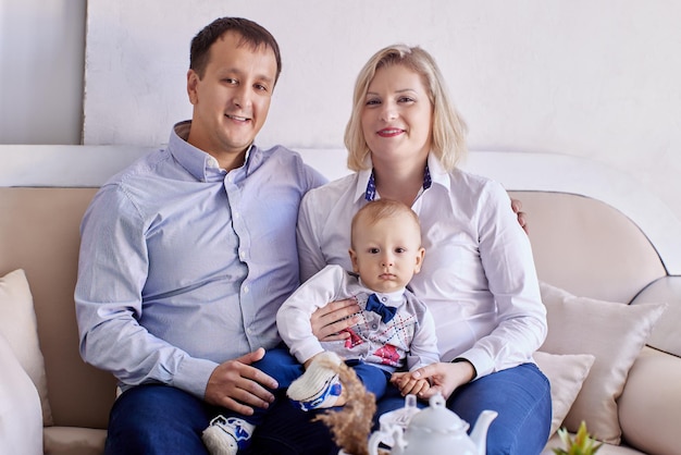 Photo toddler sits on couch with mother and father in living room