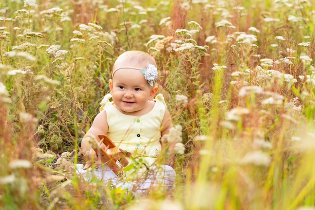 Photo toddler sits in the grass on a field among wildflowers with a wooden toy airplane in his hands