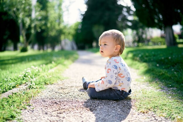 Toddler sits on the path in the park