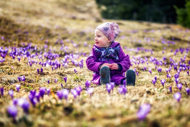 すみれ色の花でいっぱいの牧草地に座っている幼児