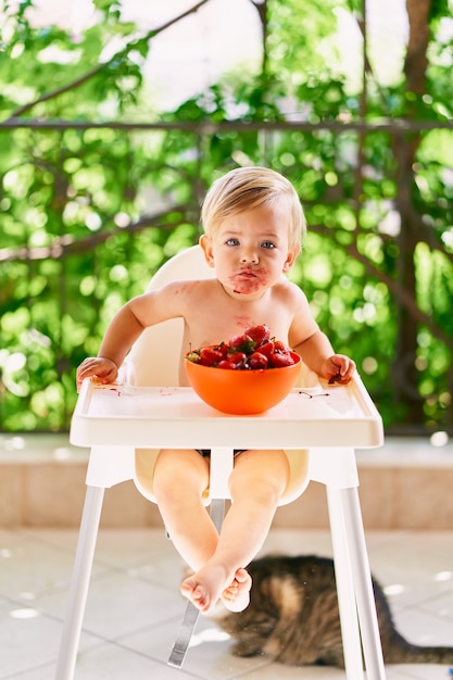 Toddler with soiled face sits on a high chair on the balcony