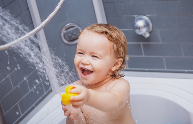 シャワーのトドラーおかしい幼児シャワーの笑顔の赤ちゃんは泡とシャボン玉の風呂で入浴します
