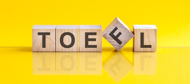 Слово Toefl, написанное на деревянном блоке. Слово предложения состоит из деревянных строительных блоков, лежащих на желтом столе. концепция образования. toefl - сокращение от теста английского как иностранного