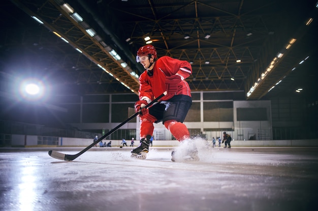 Toegewijde sterke blanke knappe hokey speler hockey spelen op ijs in de hal.