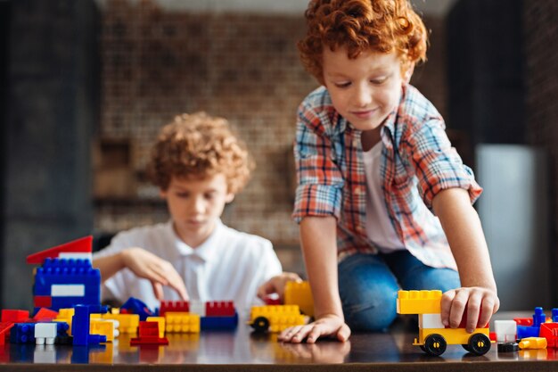 Toekomstige auto-ontwerper. Selectieve aandacht voor een kleurrijk gebouwde auto bestuurd door een schattige jongen met krullend haar die op een tafel zit en speelt