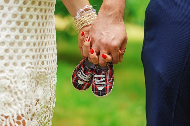 Toekomstige ouders hand in hand en een paar kleine schoenen overnature groene achtergrond.