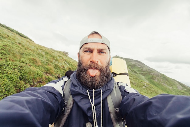 Toerisme, bergen, levensstijl, natuur, mensen, Selfie concept - Young Man Traveler maakt Selfie op achtergrond bergen In de zomer, bij zonsondergang. bebaarde toerist lacht