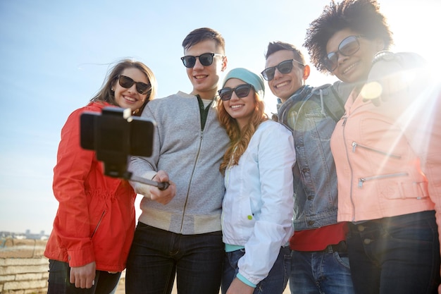 toerisme, reizen, mensen, vrije tijd en technologieconcept - groep glimlachende tienervrienden die selfie met smartphone en monopod op stadsstraat nemen