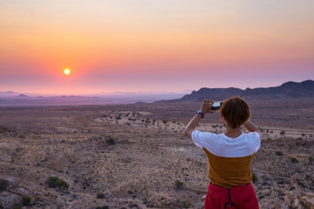 Toerist die met smartphone het overweldigende uitzicht van onvruchtbare vallei in de Namib-woestijn fotograferen