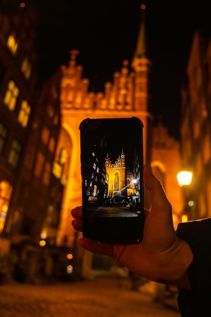 Foto toerist die met zijn mobiele telefoon een foto maakt van het stadsbeeld van gdansk met de sint-maria-basiliek en het stadhuis op