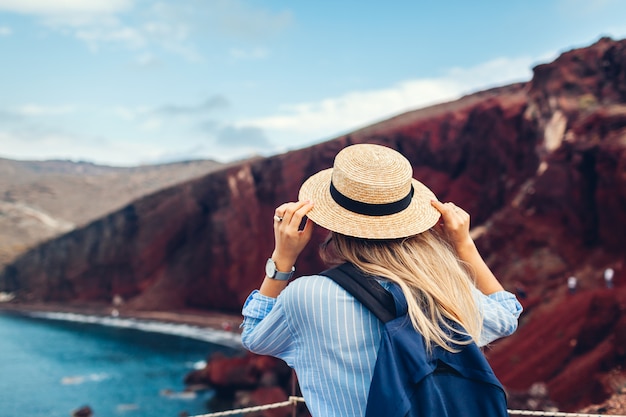 Toerist die rood strandlandschap bekijken vanaf meningspunt in akrotiri, santorini-eiland, griekenland. vrouw reizen