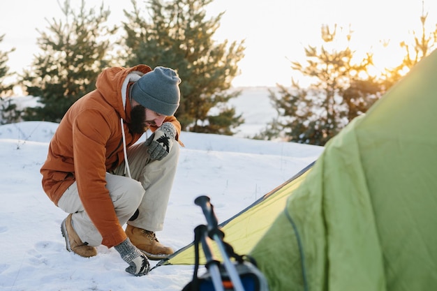 Toerist in besneeuwde bergen Een jonge man zet een tent op voor de nacht in een besneeuwd bos bij zonsondergang