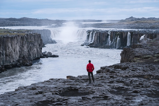 Toerist in een rode jas kijkt naar de Selfoss-waterval