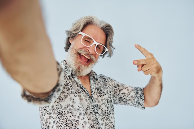 Foto toerist maakt selfie senior stijlvolle moderne man met grijs haar en baard binnenshuis