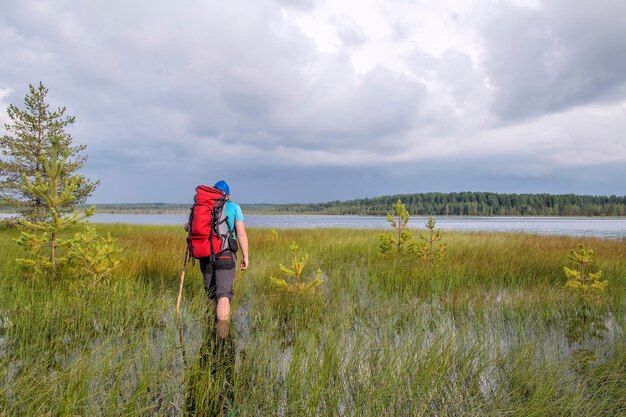 Toerist met een rugzak en een stok tijdens een wandeling waadt door overstromingen moeras naar het meer