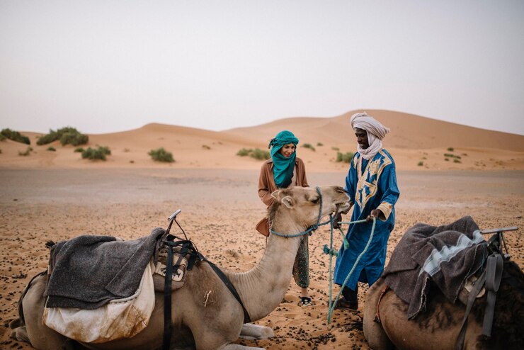 Foto toerist met gids die kameel aanraakt in de woestijn