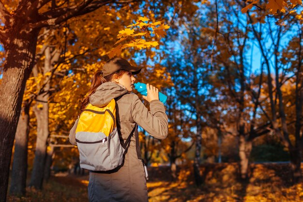 Toerist met rugzak wandelen in herfst bos. jonge vrouw drinkwater. reiziger die rust heeft