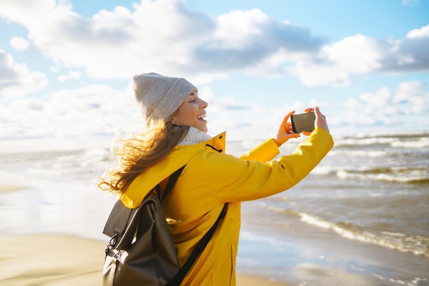 Toerist met telefoon Selfie tijd Toerist in gele jas poseren over zee bij zonsondergang Reizen