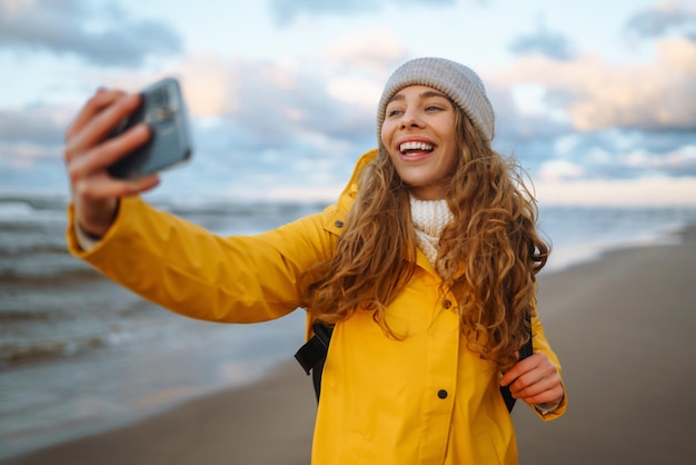 Toerist met telefoon Selfie tijd Toerist in gele jas poseren over zee bij zonsondergang Reizen