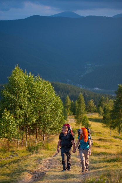 Toeristenman en vrouw die met rugzakken langs een mooi berggebied lopen, die handen houden