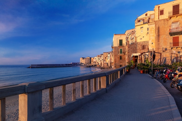Toeristenpromenade en leeg strand in oude stad van kuststad Cefalu bij zonsondergang, Sicilië, Italië