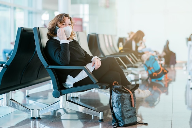 Toeristenvrouw die gezichtsmasker draagt en haar smartphoneapparaat op de luchthaven gebruikt