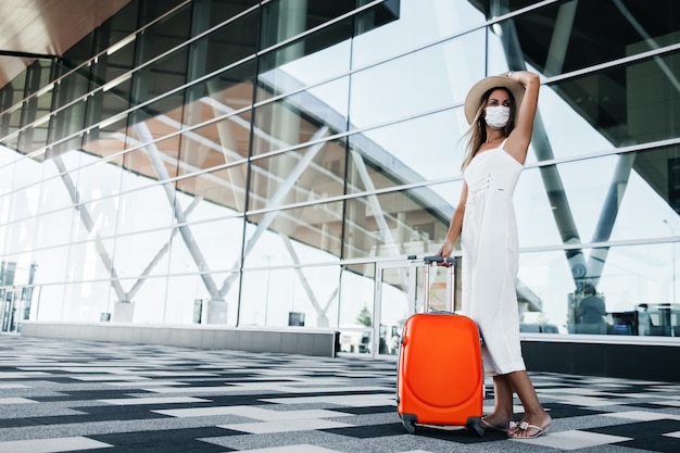 Foto toeristenvrouw in gekke masker die zich met bagage dichtbij luchthavengebouw bevinden