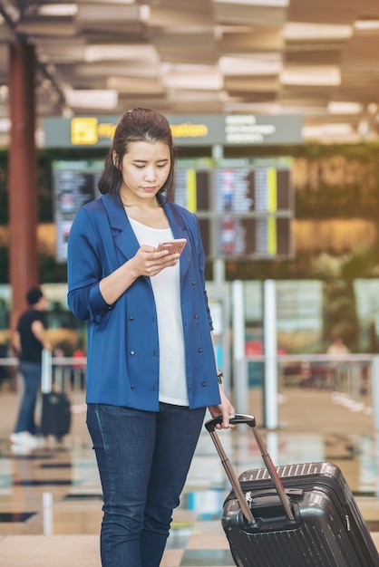 Toeristenvrouw met bagage in de luchthaven. Gelukkige jonge reiziger met mobiele telefoon.