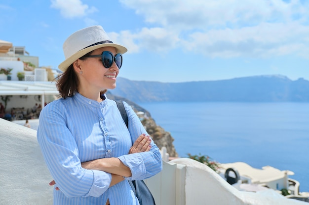 Toeristisch bedrijf, zelfverzekerde zakenvrouw, eigenaar met gevouwen armen die de achtergrond van het landschap van het dorp Oia op het eiland Santorini poseert, kopieer ruimte